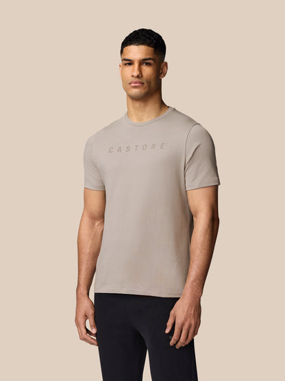 Male model wearing a beige Rock Grey graphic lifestyle T shirt with a Castore logo across the chest.