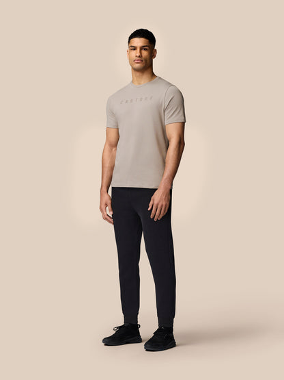Male model wearing Rock Grey graphic lifestyle T shirt with Castore logo, paired with black joggers and sneakers.