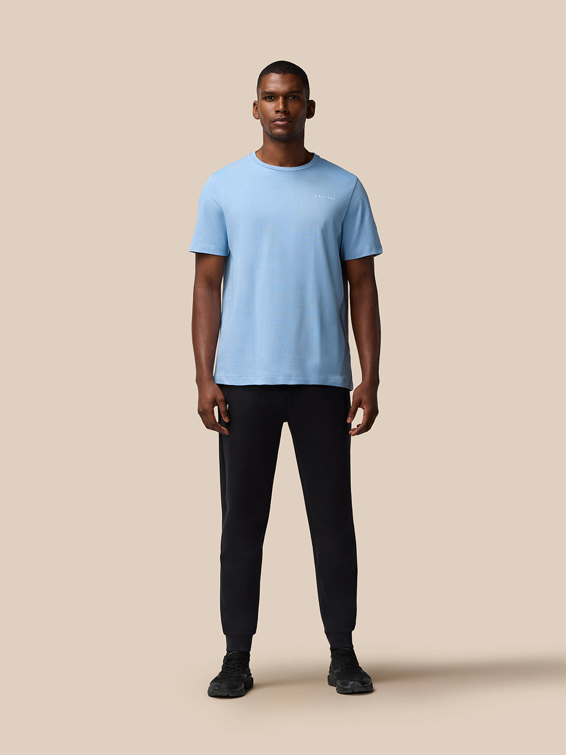 Full body view of a model in a sky blue graphic training T shirt with black pants against a beige background