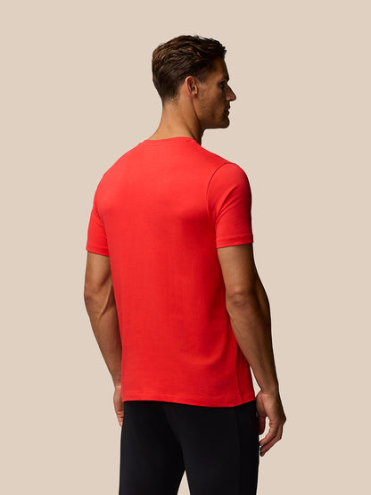 Back view of a man wearing a bright poppy red graphic training T-shirt against a beige background