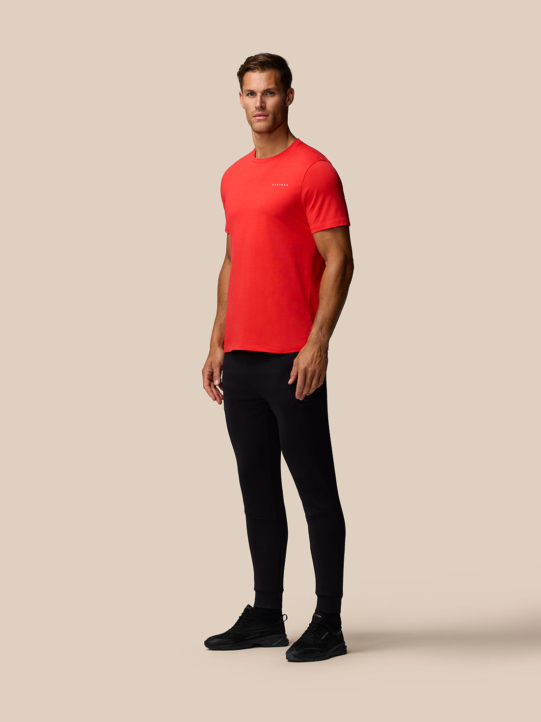 Three quarter front view of a man in a red graphic training T-shirt with a small white chest logo against a beige backdrop