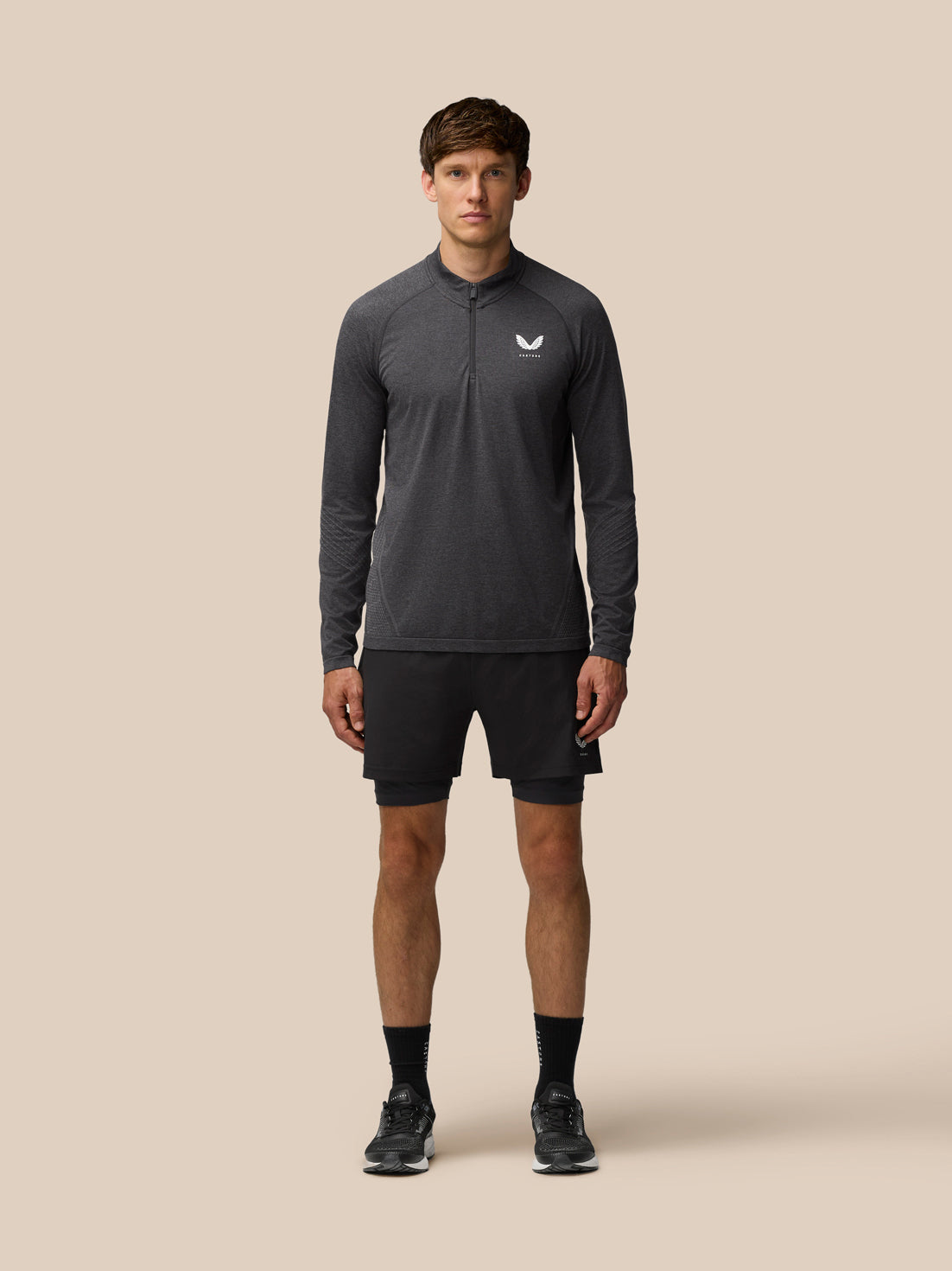 Full-body front view of a male model wearing a dark gray Flow Training 1/4 Zip Top with chest zipper and Castore logo against a neutral background