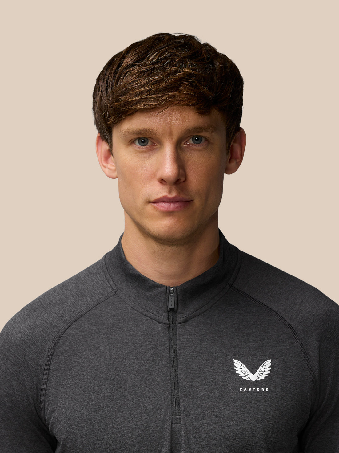 Close-up of a male model in a dark gray Flow Training 1/4 Zip Top showing the front zip and Castore logo on the chest