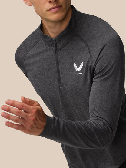 Shoulder and chest close-up of a male model wearing the Flow Training 1/4 Zip Top in dark charcoal highlighting the Castore emblem on the left chest