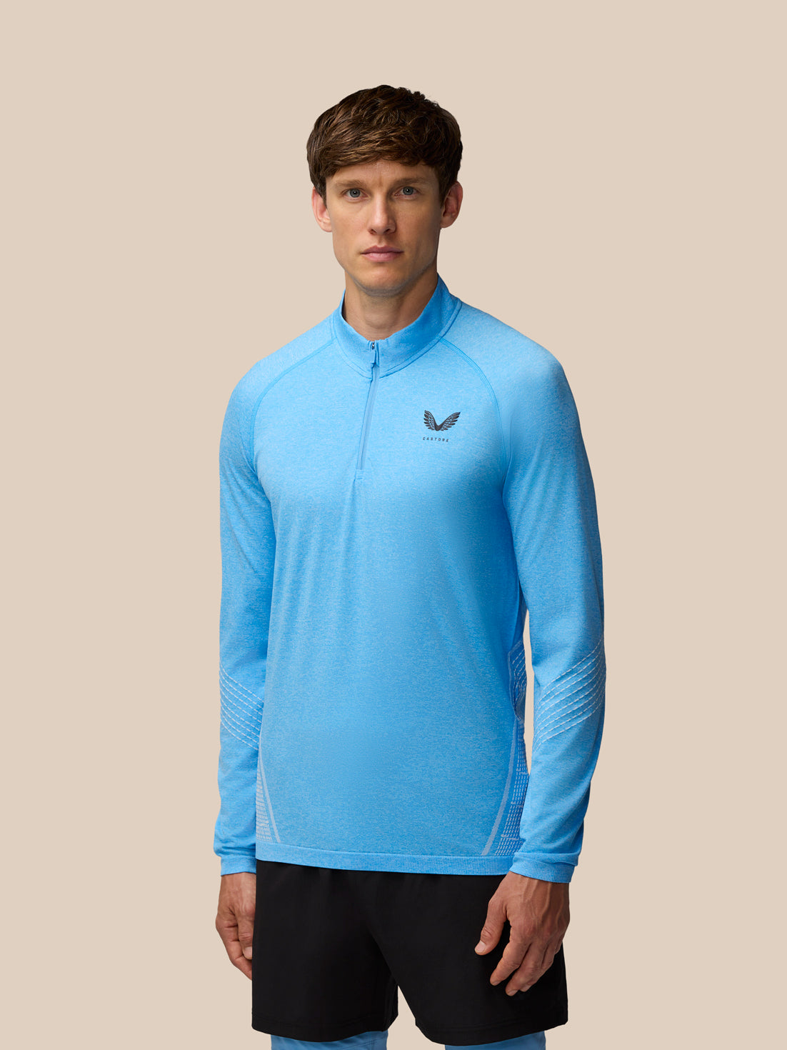 Male model wearing cool blue Flow Seamless quarter zip long sleeve top with left chest Castore logo.
