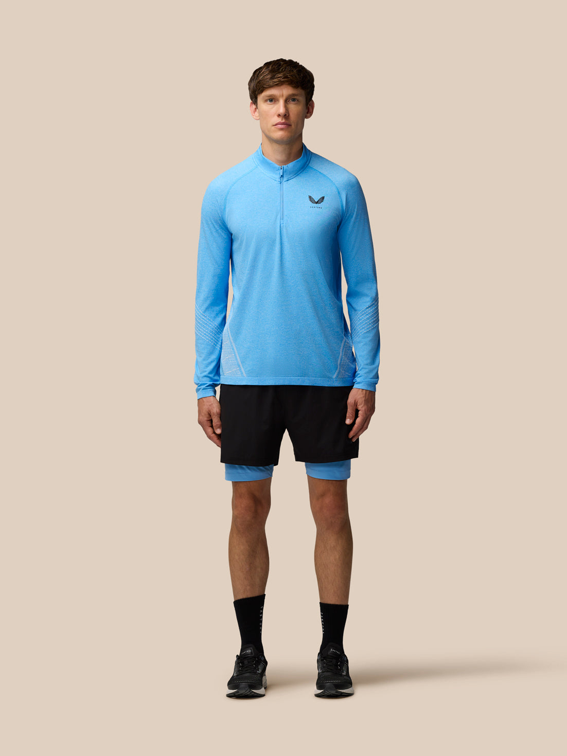Full body view of a model in Flow Seamless Quarter Zip Long Sleeve Top in cool blue with black shorts.