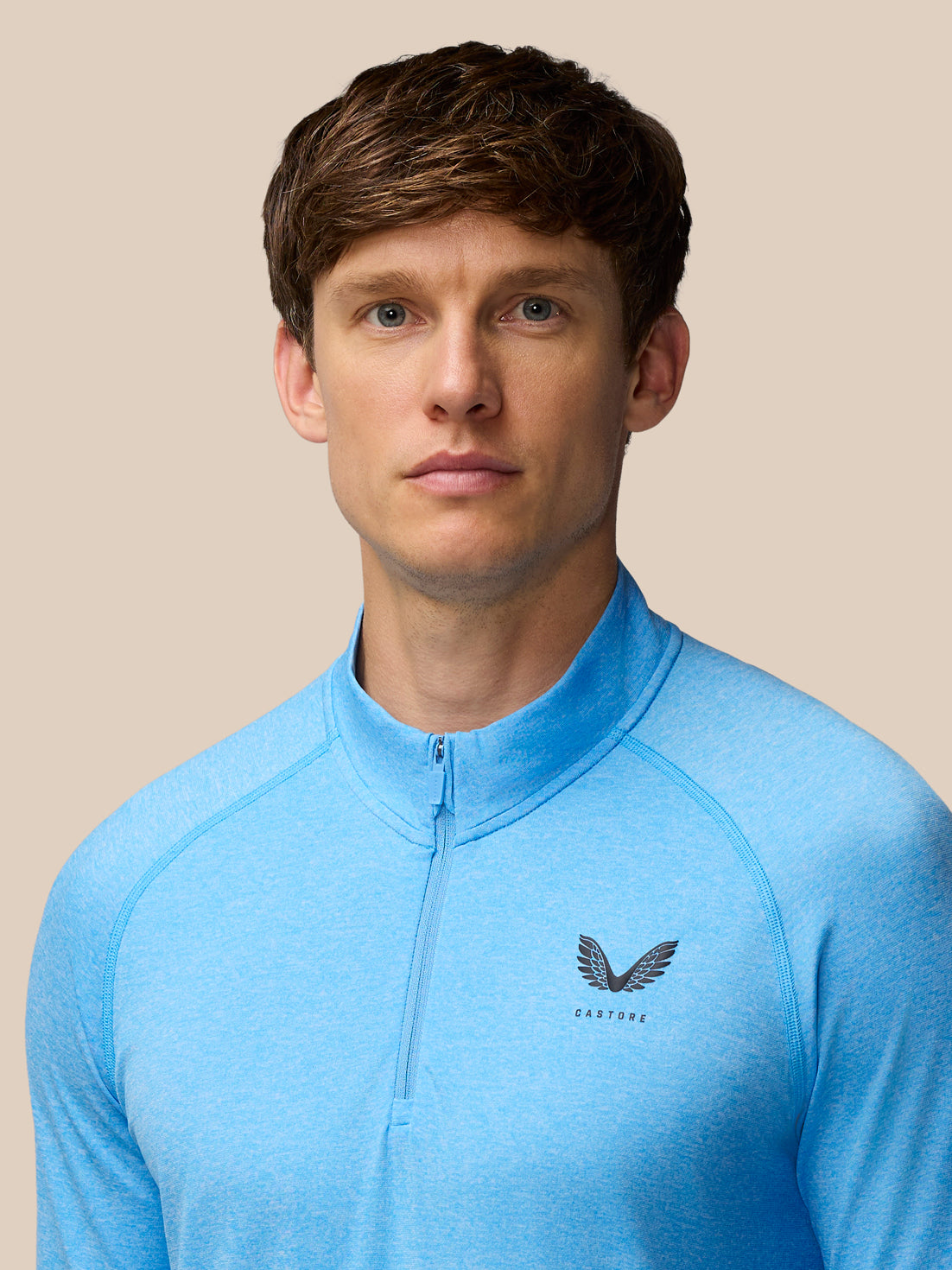 Model wearing Flow Seamless Quarter Zip Long Sleeve Top in cool blue with funnel collar and Castore logo on chest.
