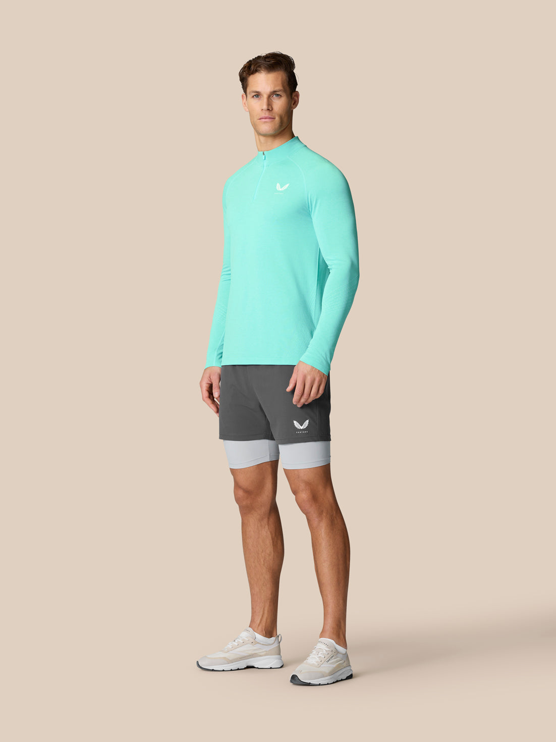 Male model in light aqua Flow Training 1/4 Zip Top three-quarter front view highlighting branding and athletic fit.