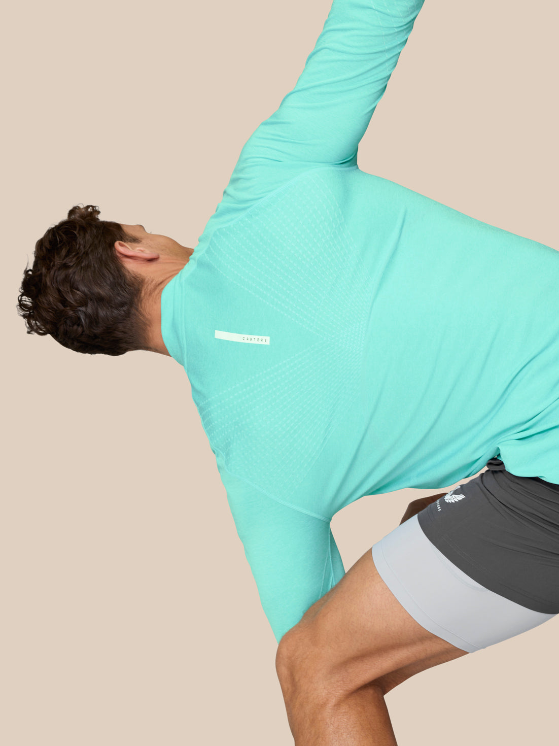 Male model wearing light aqua Flow Training 1/4 Zip Top, back view shown with seamless fabric and knit panels during a stretch.