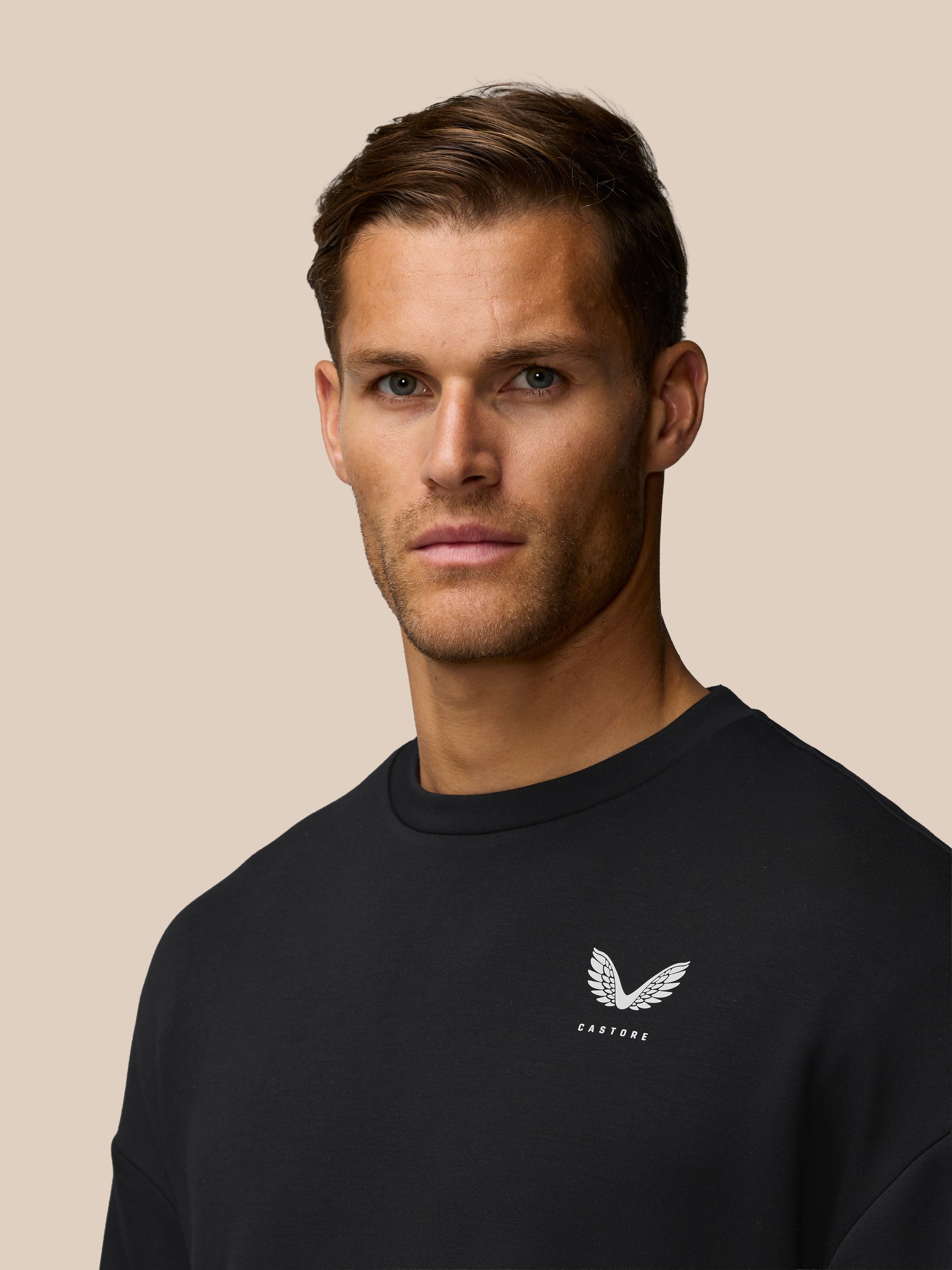 Close up of a man in a black Crew Neck Sweatshirt with a white wing crest logo on the chest