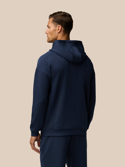 Back view of a man in navy Travel Lifestyle Zip Hoodie showing the hood and relaxed fit.