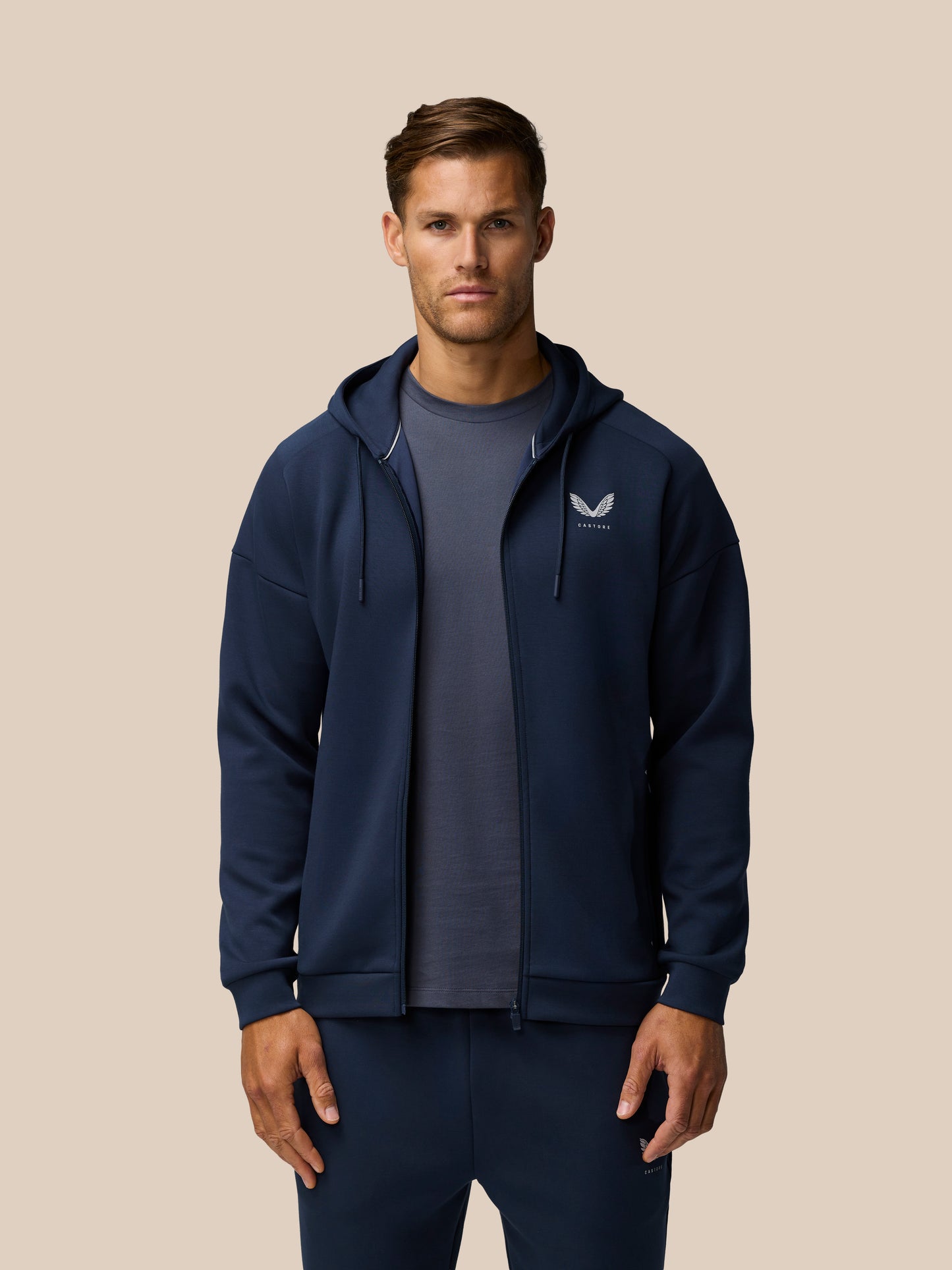 Man in navy Travel Lifestyle Zip Hoodie facing forward with Castore logo on the left chest.