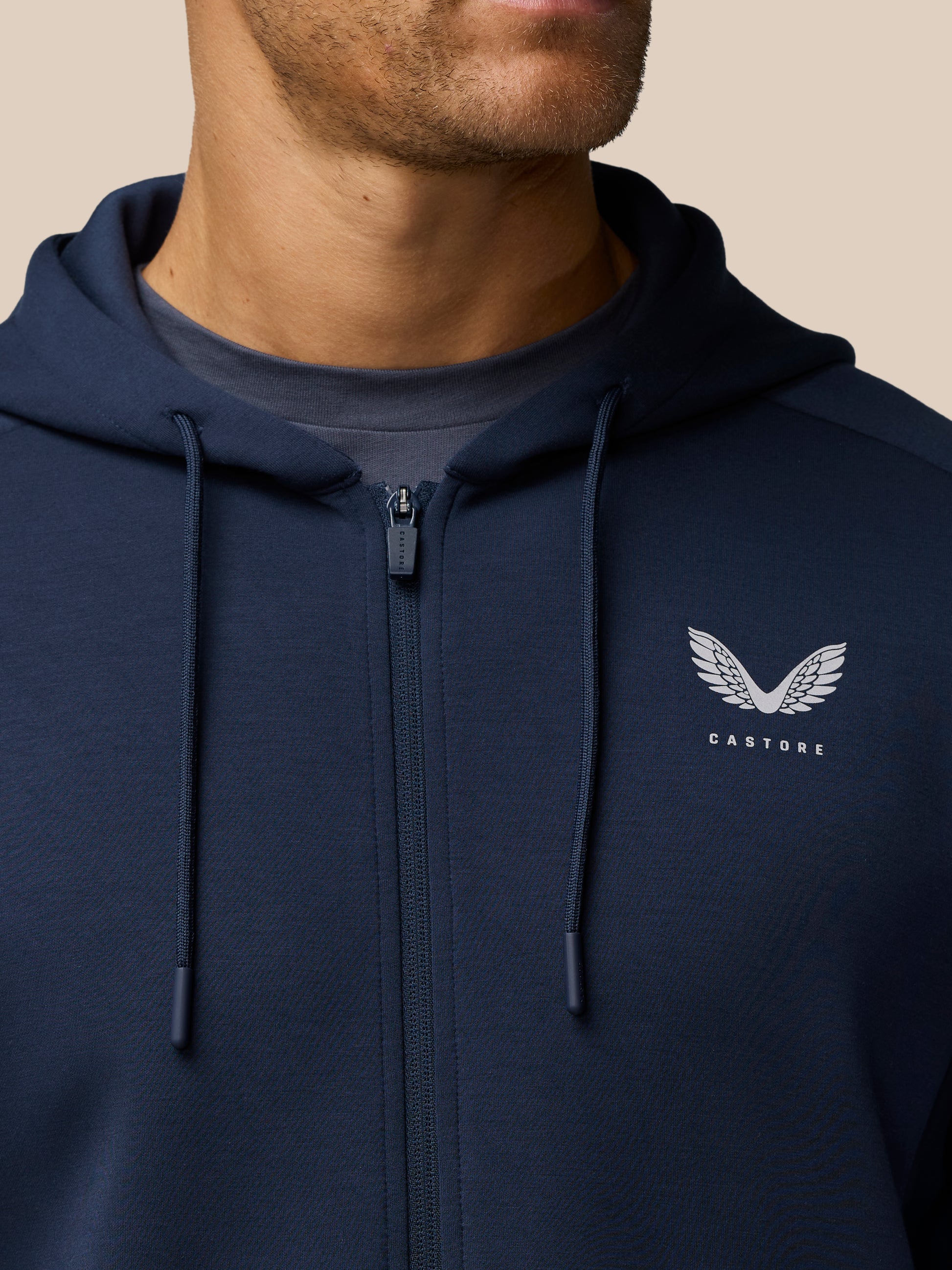 Close-up of navy Travel Lifestyle Zip Hoodie showing zipper drawstrings and Castore logo on the chest