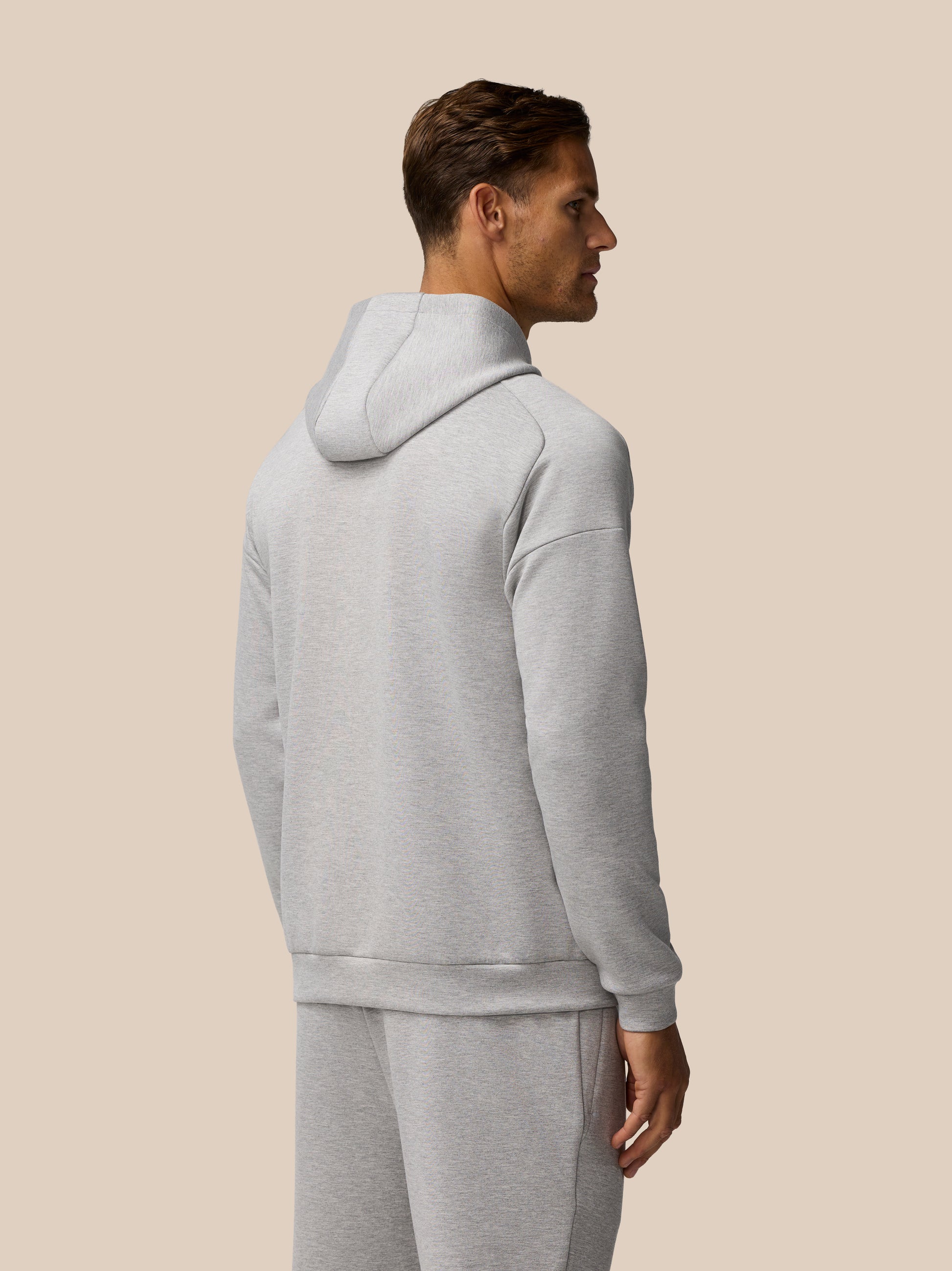 Back and side view of a man wearing a grey marl Travel Lifestyle Hoodie with hood down.