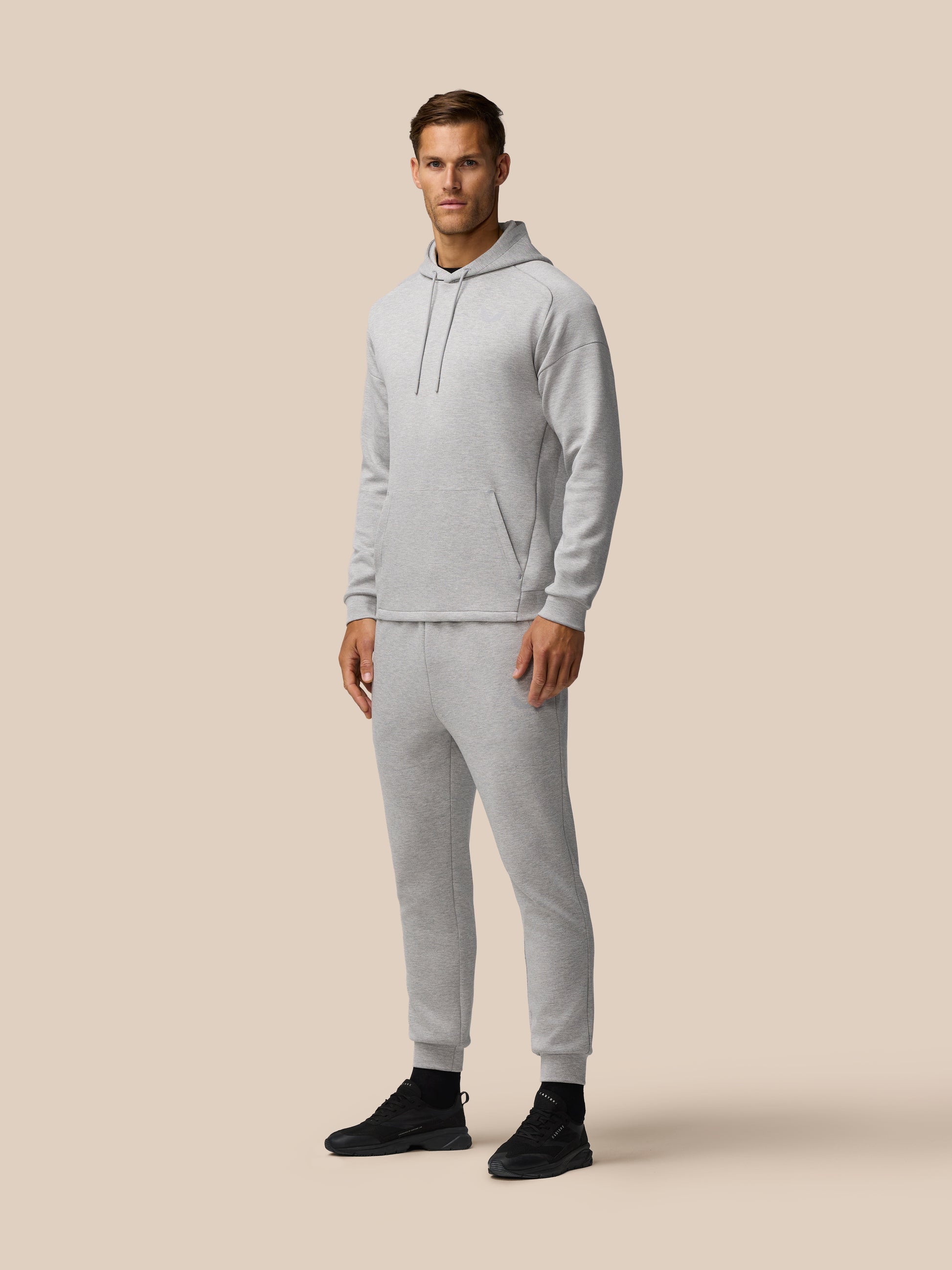 Model wearing light grey marl travel hoodie with hood and front kangaroo pocket against a beige backdrop