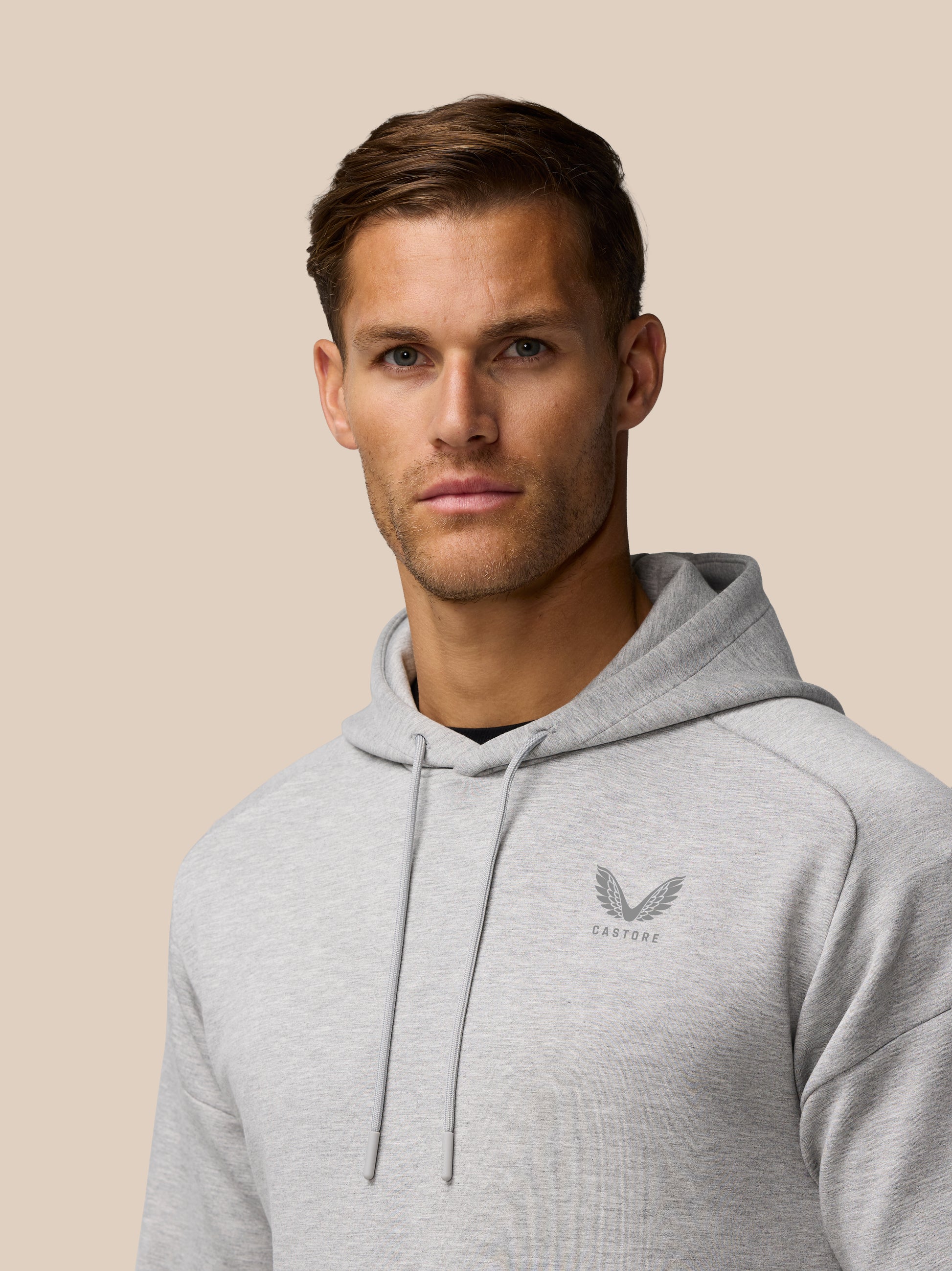 Side profile of a man in a grey marl Travel Lifestyle Hoodie with hood and chest logo.