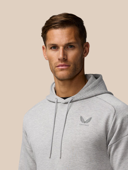 Side profile of a man in a grey marl Travel Lifestyle Hoodie with hood and chest logo.