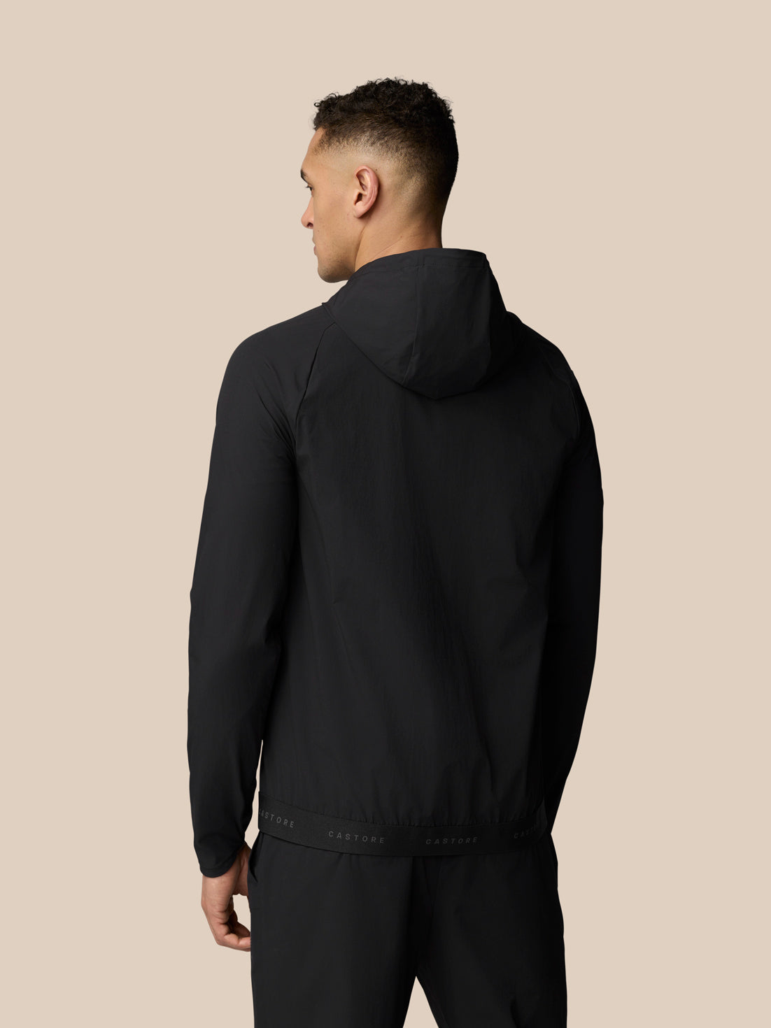 Back view of man in black Adapt Wind Jacket with hood and CASTORE branded waistband