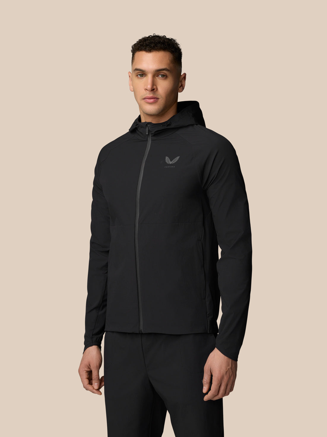 Full-body view of a man wearing a black hooded wind jacket with front zip