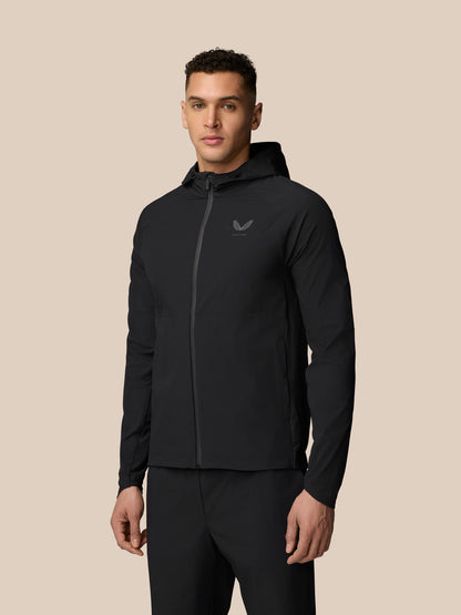 Full-body view of a man wearing a black hooded wind jacket with front zip