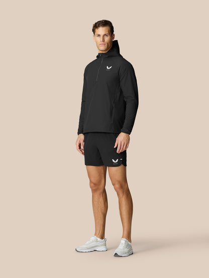 Full body shot of male model in black Flow half zip Hoodie with hood up, logo on chest, paired with black shorts and white sneakers.