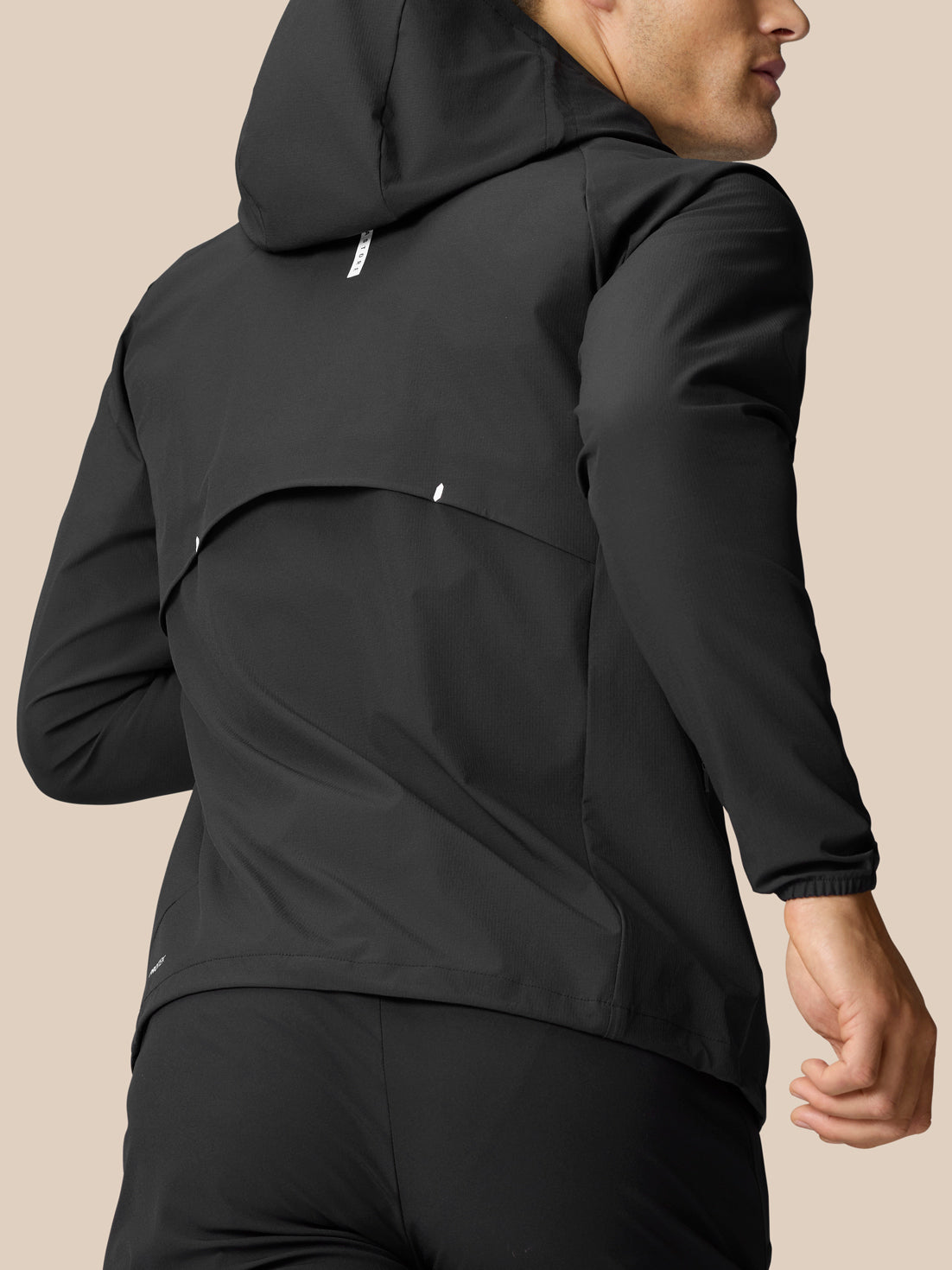 Back view of a man in a black Flow training hoodie with hood up, showing the curved panel detail and relaxed fit.