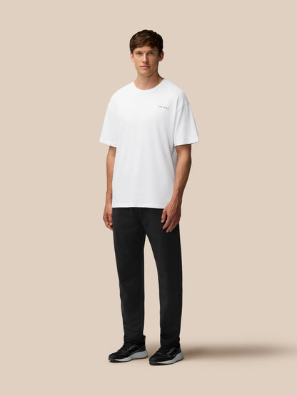 Male model wearing a white oversized T shirt with black tailored trousers against a beige studio backdrop
