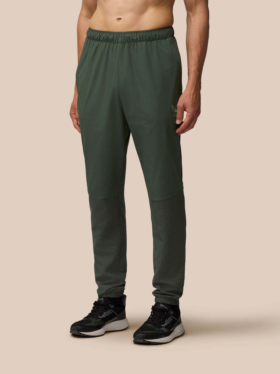Dark green Flex Winterised Woven Joggers on a male model with an elastic waistband, tapered legs, and textured lower leg panels paired with black sneakers.