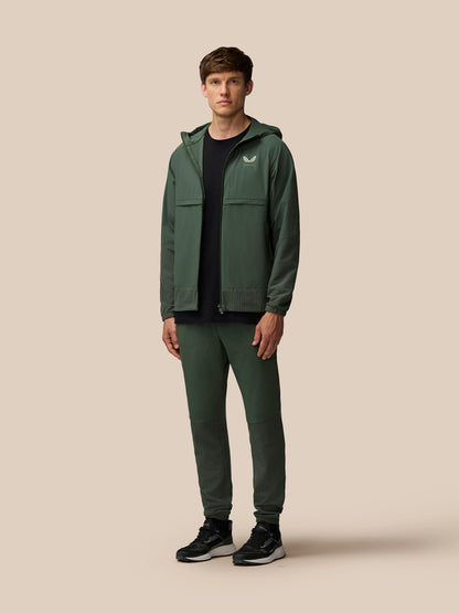 Full-length model in a dark green Castore Flex Winterised Woven outfit wearing a jacket and matching joggers.