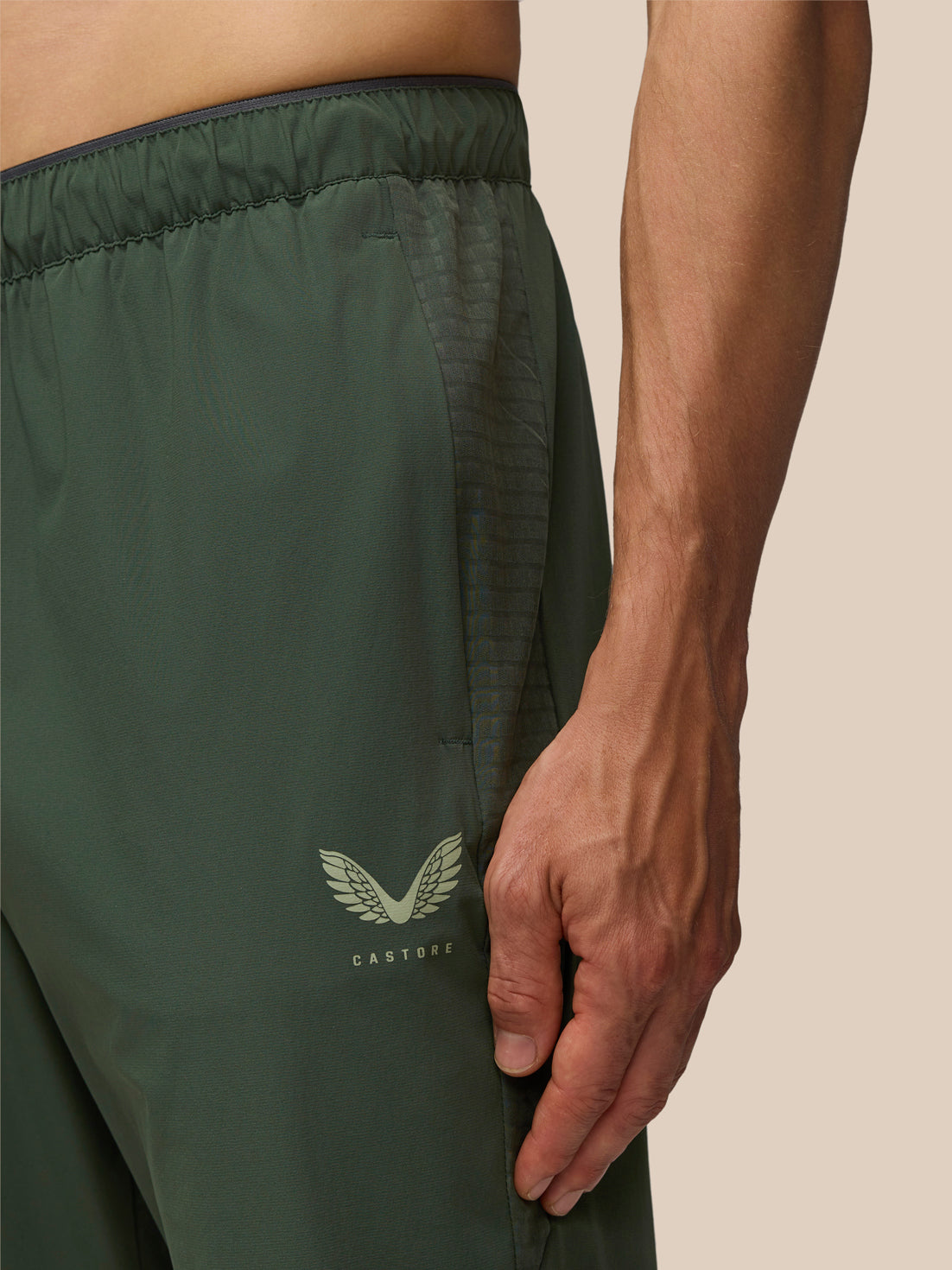 Close-up of the waistband and leg showing a textured panel and Castore logo on the dark green joggers.