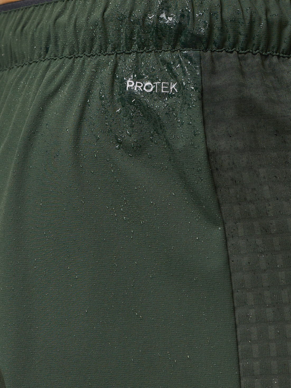 Close-up of dark green Flex Winterised Joggers fabric showing an elastic waistband and ProTek branding with water droplets.