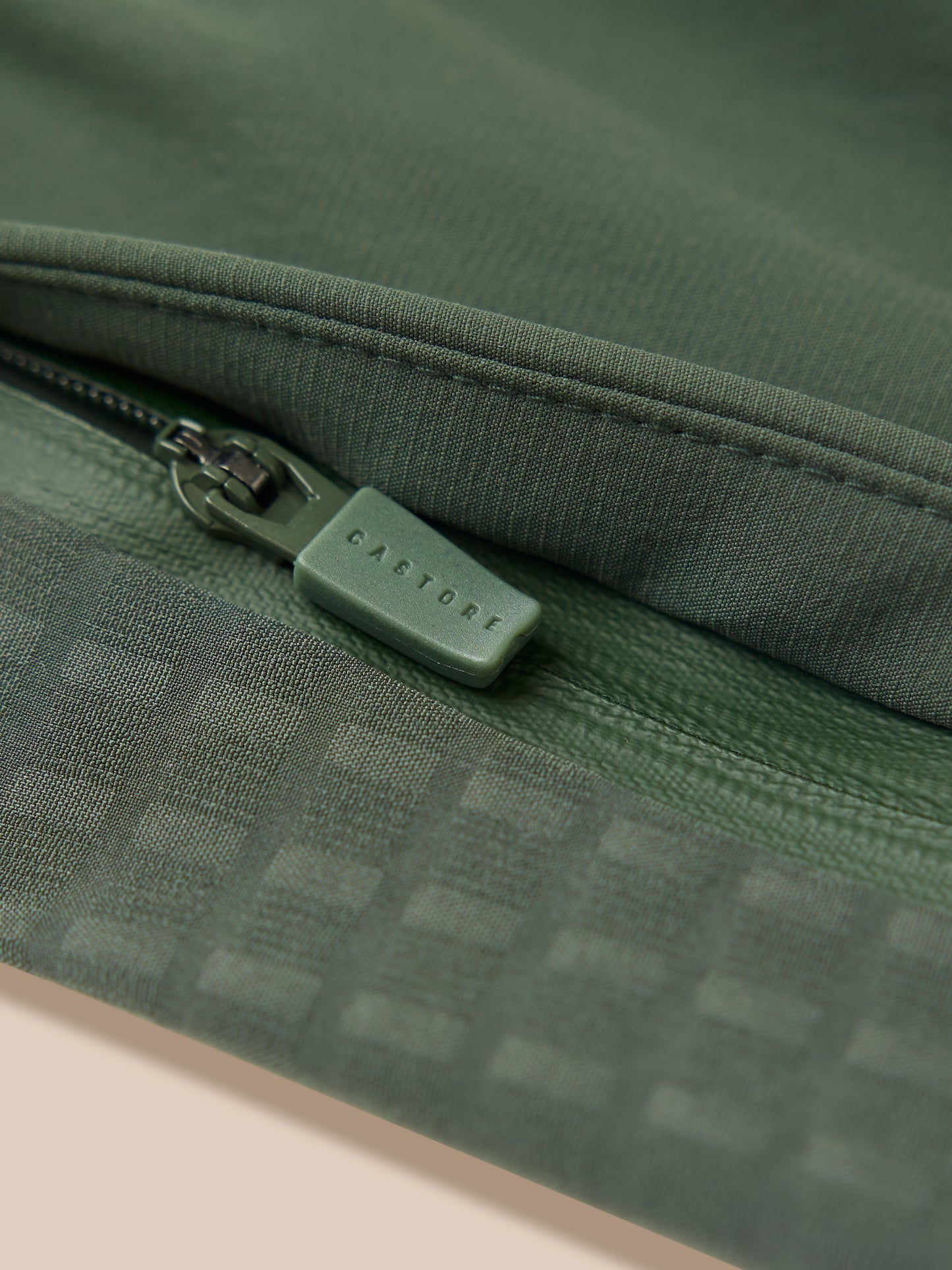 Close up of dark green woven fabric with a green zipper pull featuring Castore branding