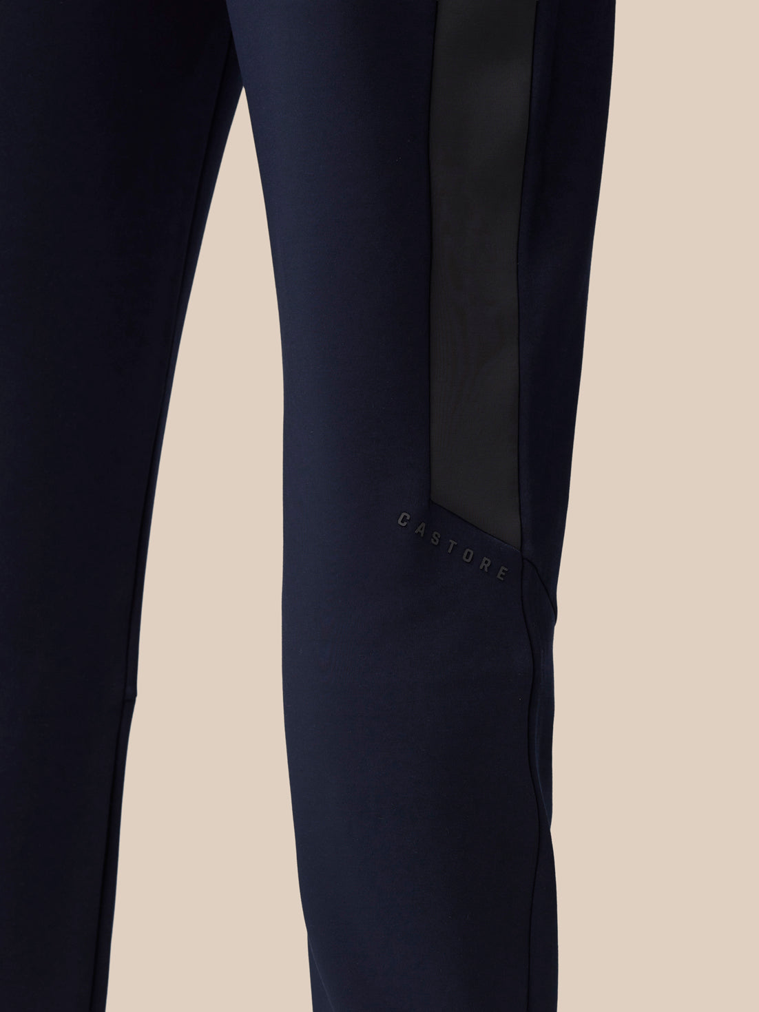 Close-up of navy pant leg with a dark side stripe and Castore branding near the knee.
