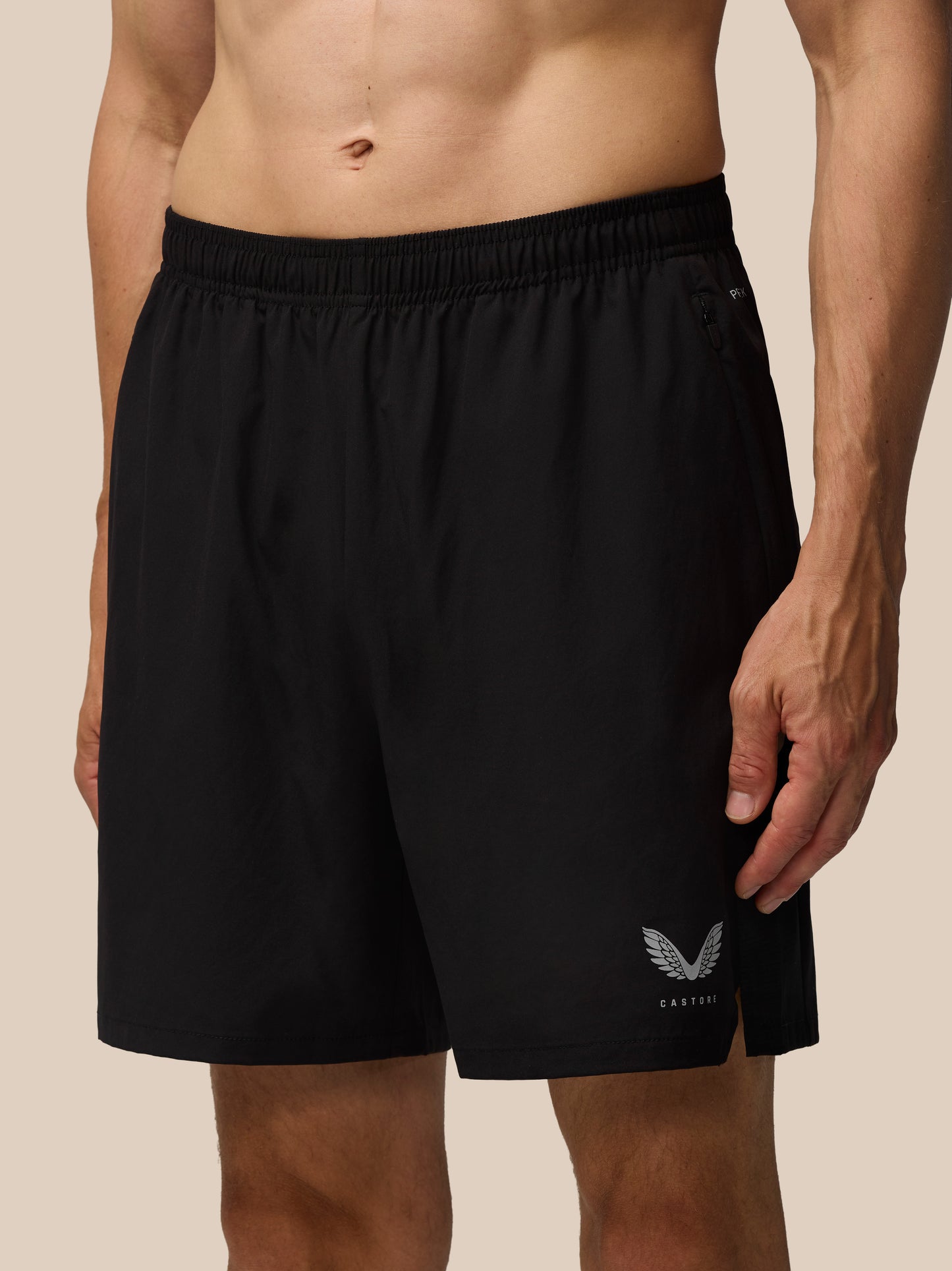 Close up of black Apex Training 6 inch shorts showing elastic waistband, side zip pocket, and Castore wing logo at the hem.