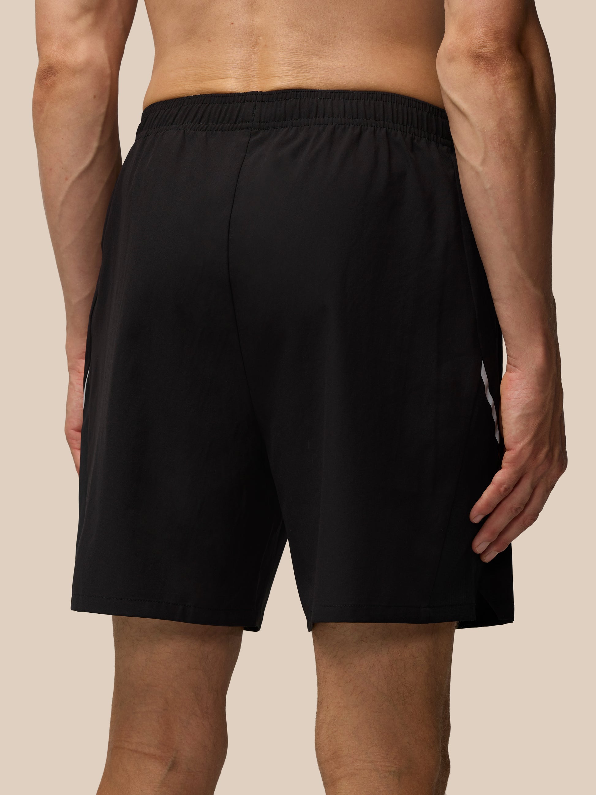 Back view of a male model wearing Apex Training 6 inch shorts in black with an elastic waistband and white side stripe.