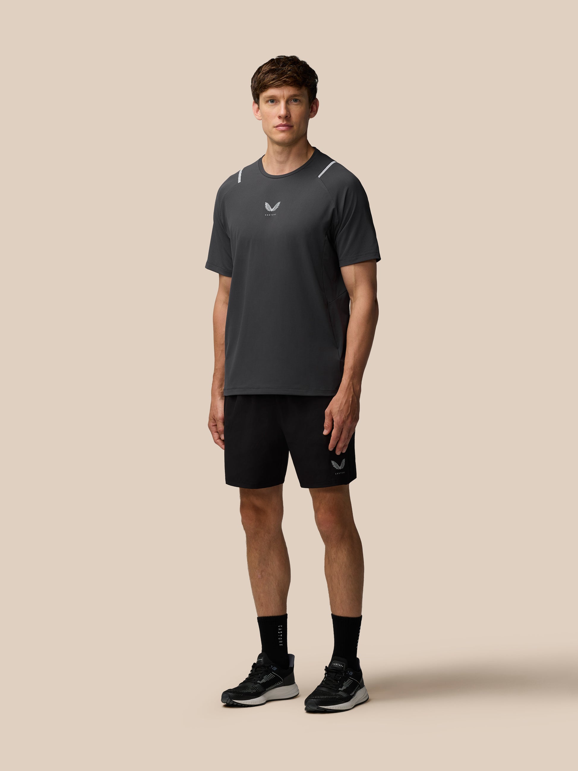 Model wearing Apex Training 6 inch Shorts in black with logo on the left leg against a beige background.