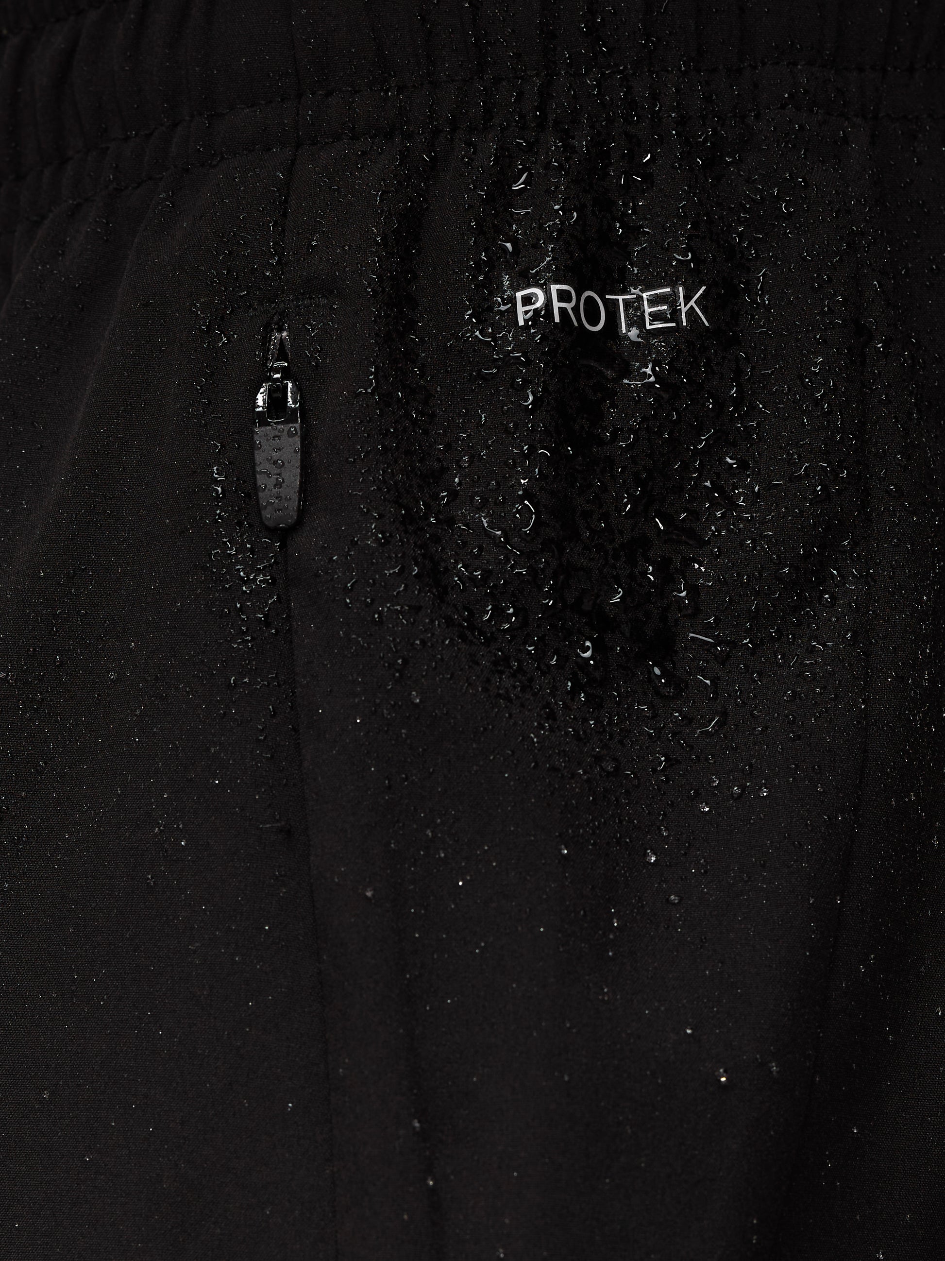 Close up of black Apex Training 6in shorts fabric with ProTek branding and a zipper pocket with water droplets