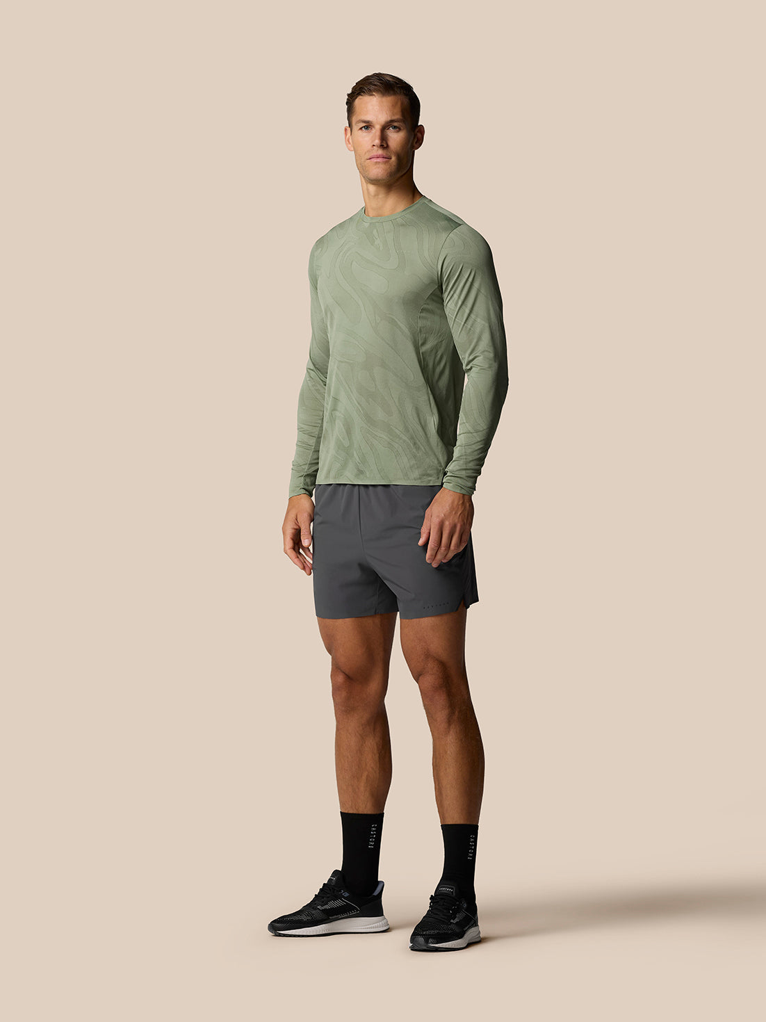 Full-body view of a man wearing a green patterned long-sleeve top and gunmetal Zone Training LVS shorts