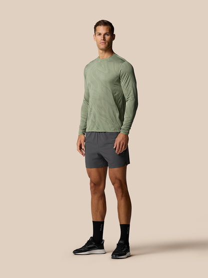 Full-body view of a man wearing a green patterned long-sleeve top and gunmetal Zone Training LVS shorts
