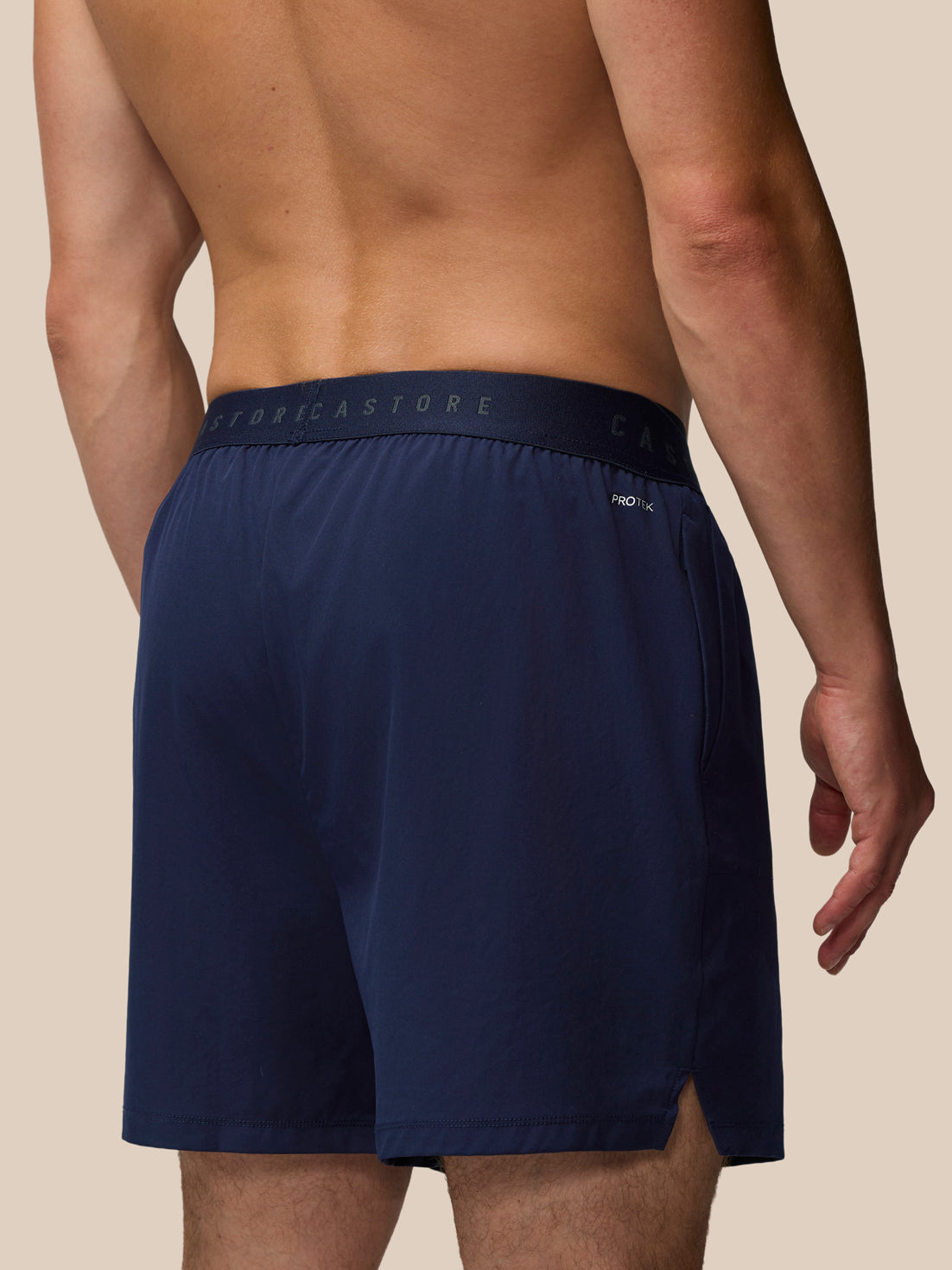 Back view of a man wearing navy Adapt Training 5 Inch Shorts with an elastic waistband and ProTek branding.