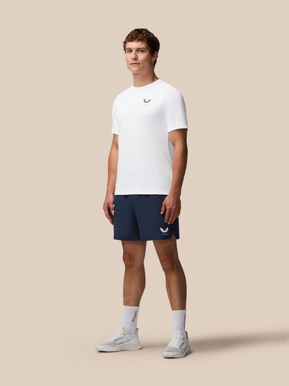 Full body shot of male model in white T shirt and navy Adapt Training 5-Inch Shorts with Castore logo on the shorts