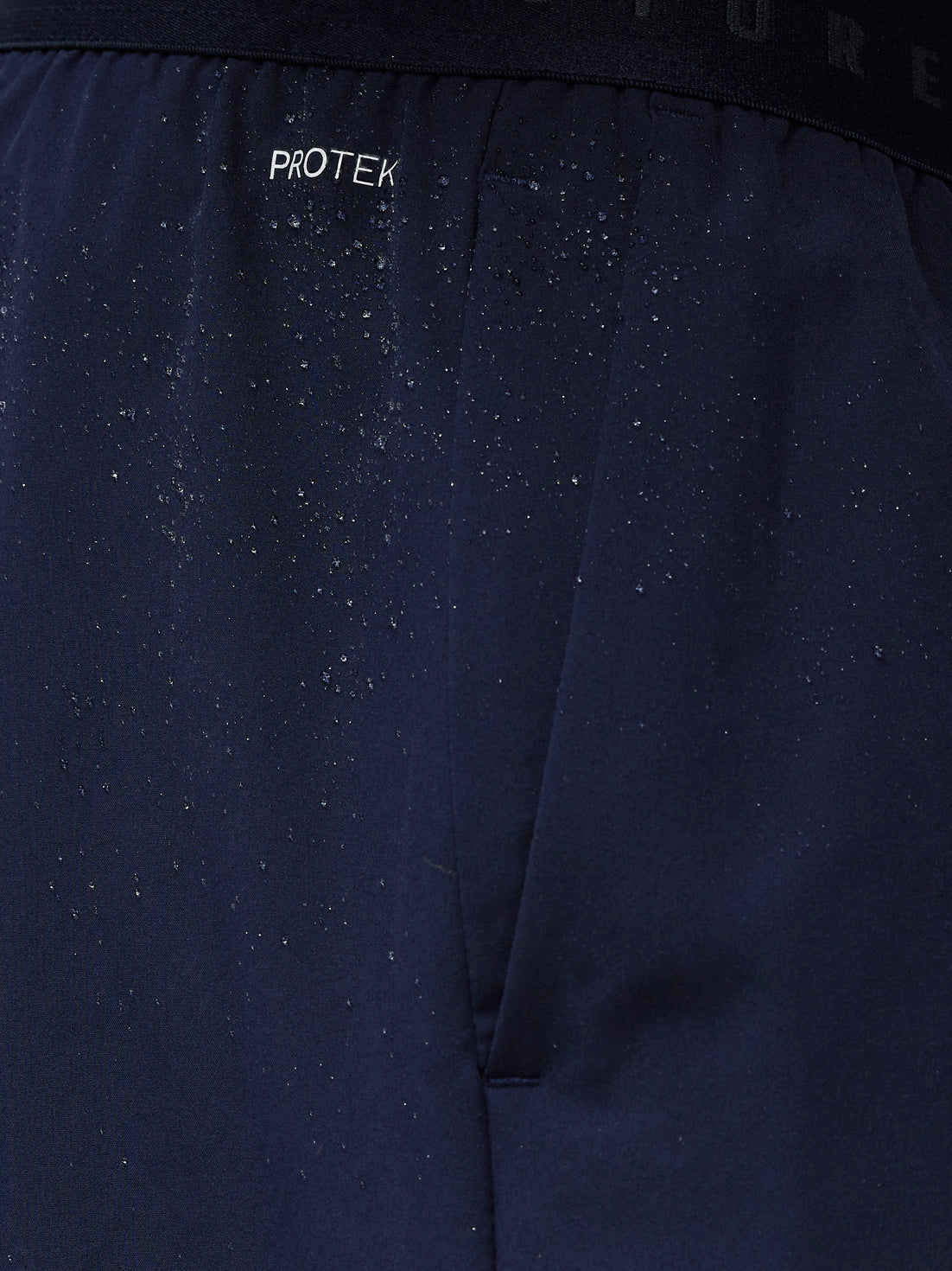 Close-up of navy shorts waistband showing ProTek branding and water droplets on the fabric.