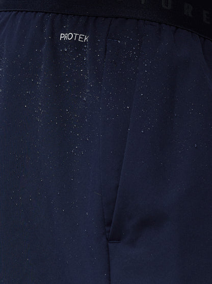Close-up of navy shorts waistband showing ProTek branding and water droplets on the fabric.