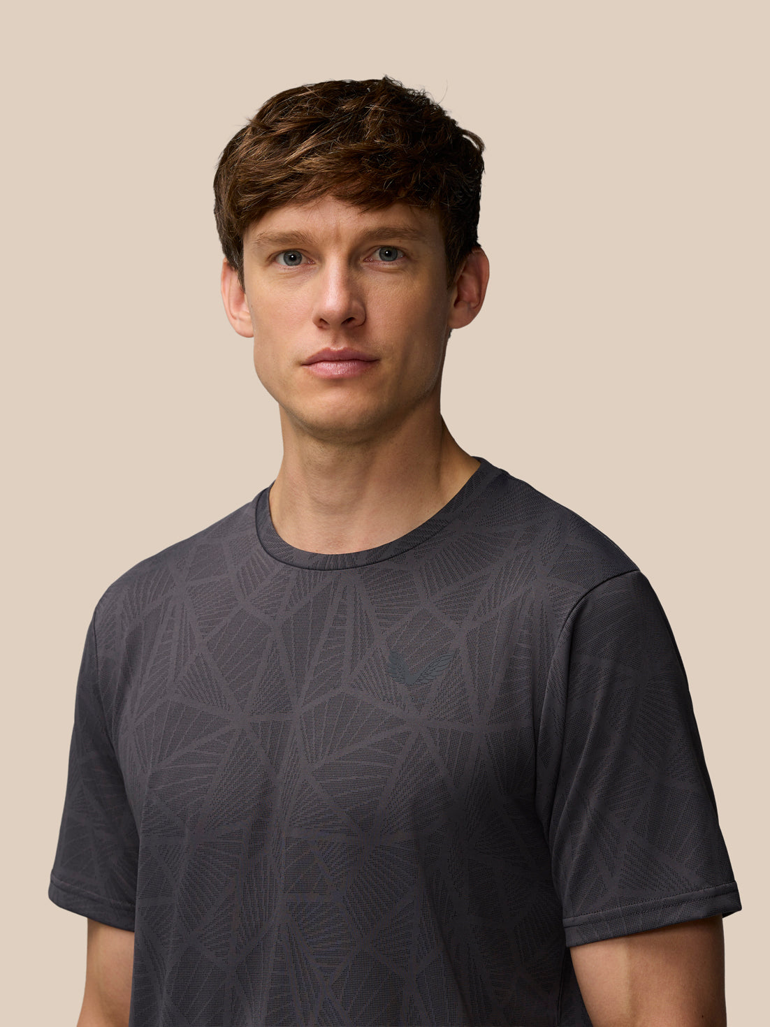 Man wearing Flow Training Engineered Knit T-Shirt in dark gray with geometric knit pattern and Castore logo on chest