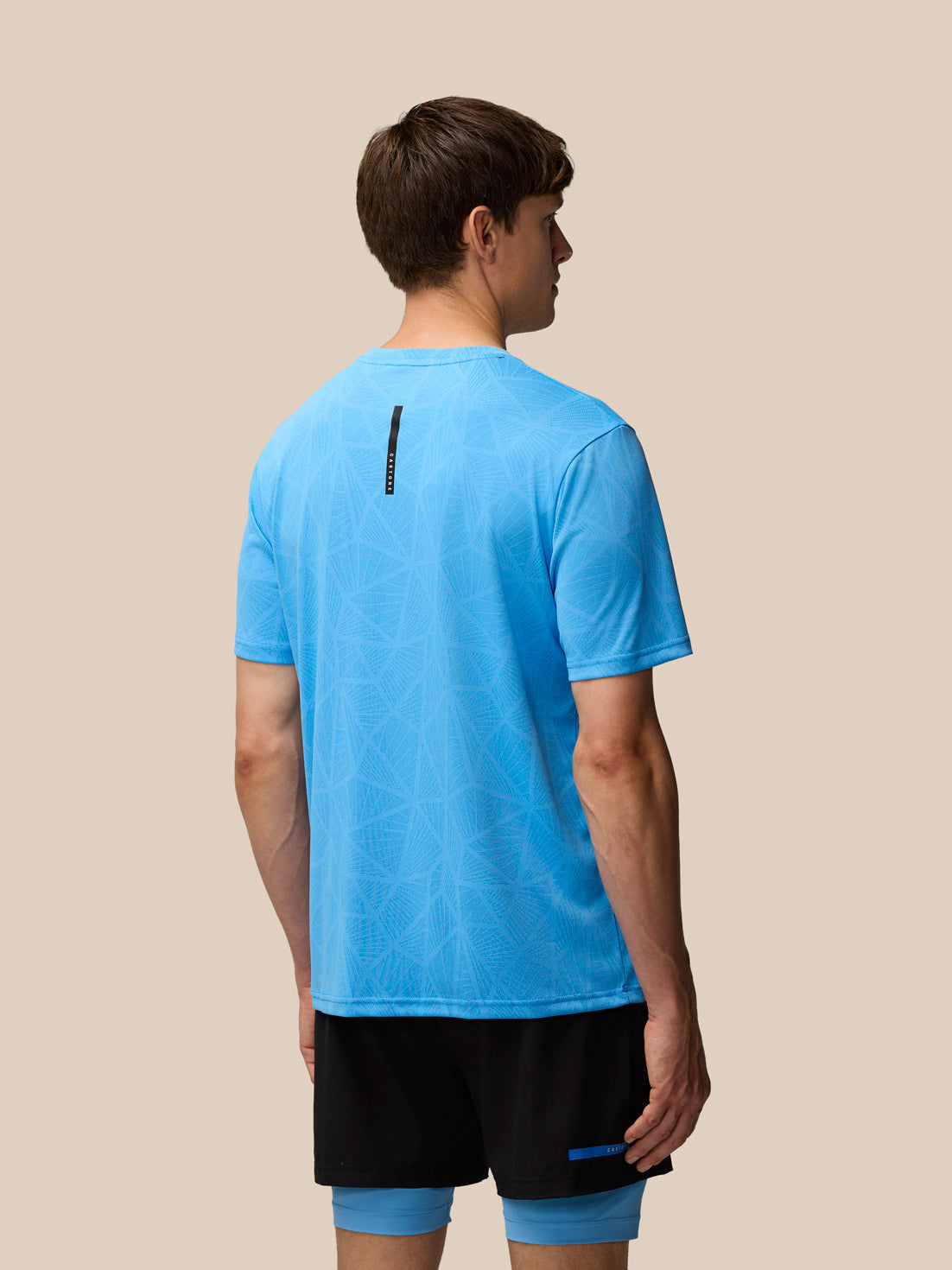 Back view of a man wearing a light blue Flow Training Engineered Knit T Shirt with geometric knit and branded back neck tape.