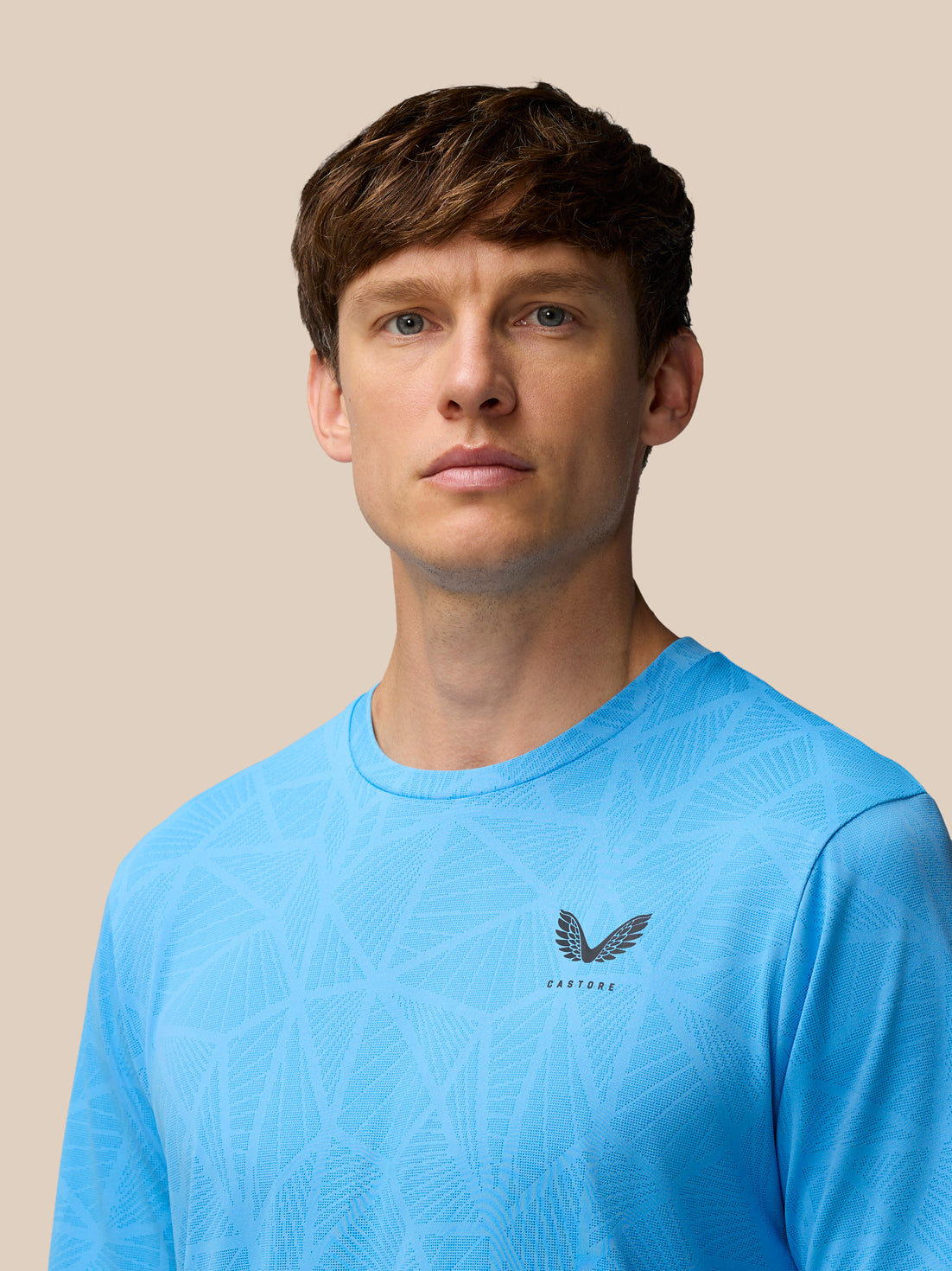 Front view of a man wearing a light blue Flow Training Engineered Knit T Shirt with geometric knit pattern and Castore logo on the left chest.