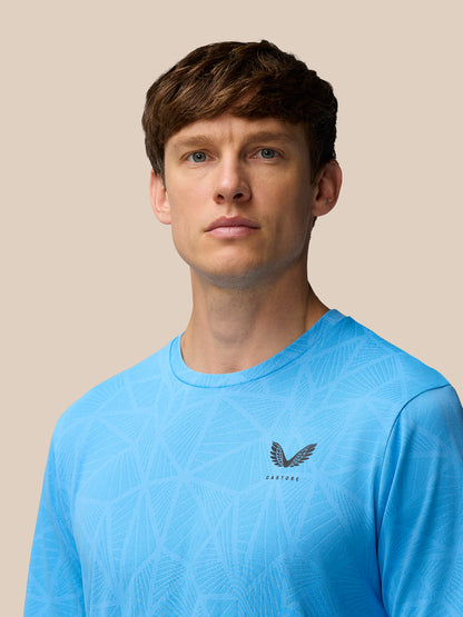 Front view of a man wearing a light blue Flow Training Engineered Knit T Shirt with geometric knit pattern and Castore logo on the left chest.