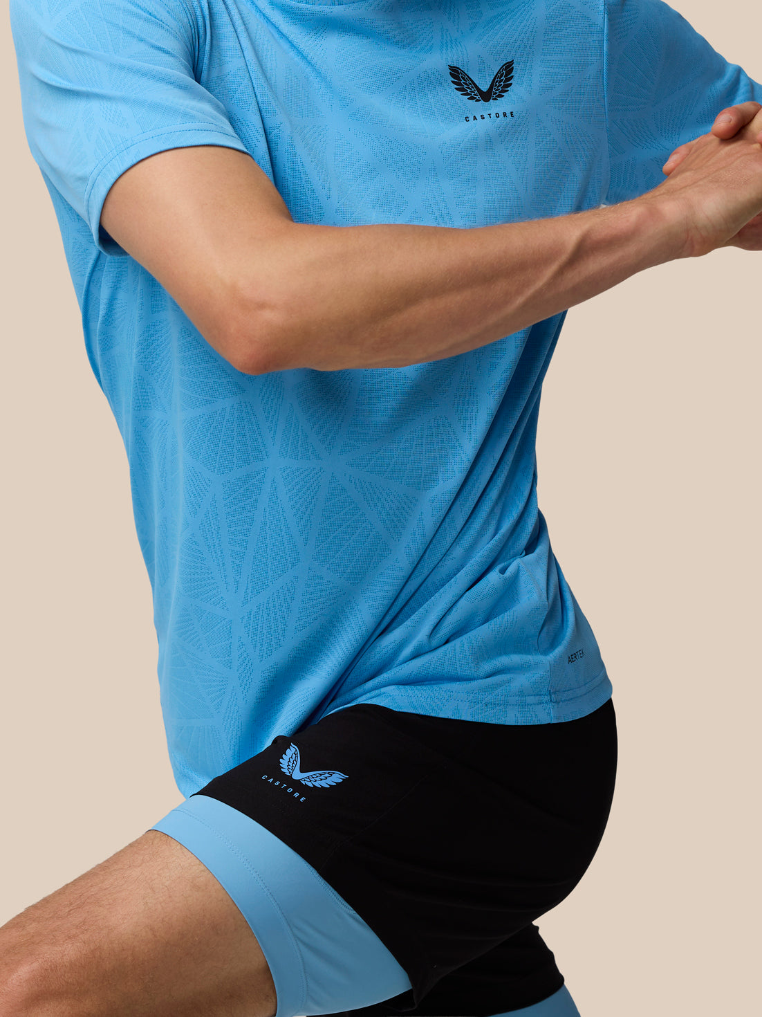 Side view of a man in a light blue Flow Training Engineered Knit T Shirt with Castore logo on the left chest and geometric knit pattern.