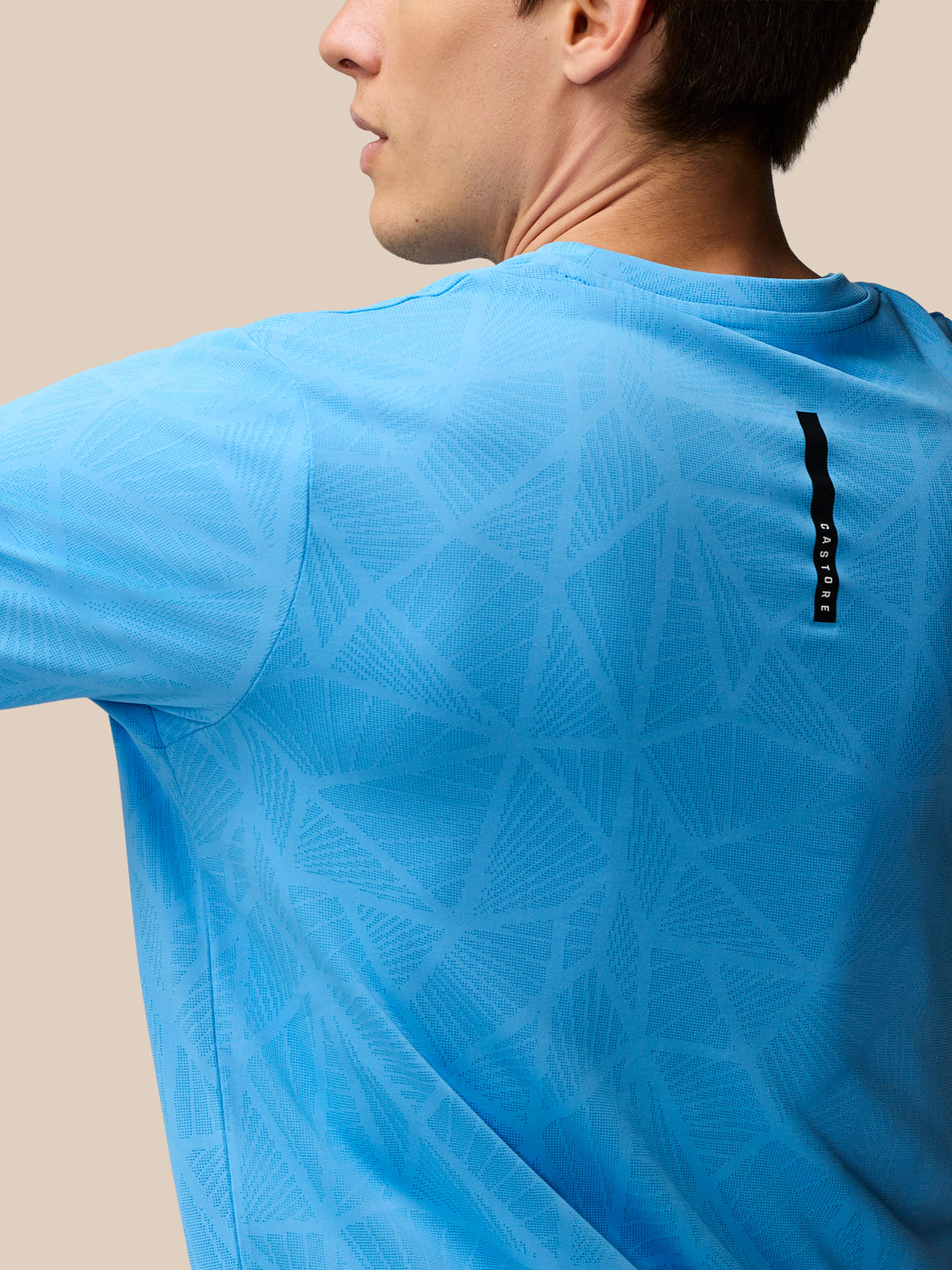Back view of Flow Training Engineered Knit T Shirt in cool blue with geometric knit pattern and branded back neck tape