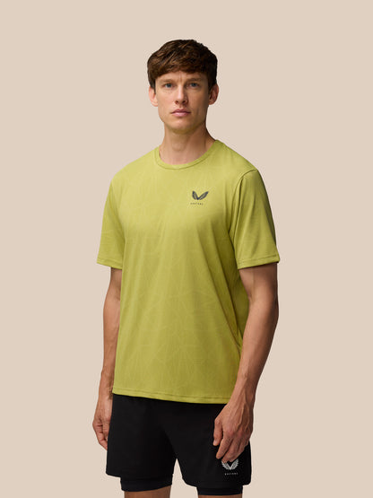 Front view of Flow Training Engineered Knit T-Shirt in Mustard on male model with black shorts, Castore logo on left chest, beige backdrop.